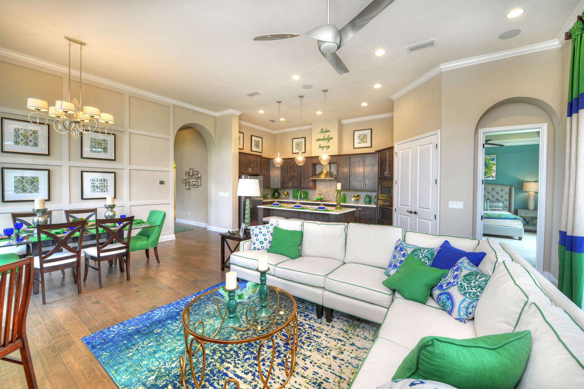 A living room with beige sofa, brown chairs, fireplace, TV, and large windows. Part of a luxury, model home.